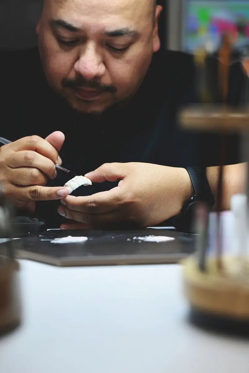 Artist focusing on detailed sculpting work with tools and materials on a workspace.